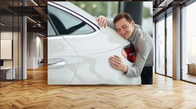 Close up of adult content caucasian man being completely satisfied with his new car, hugging it with eyes closed and leaning on car bonnet Wall mural