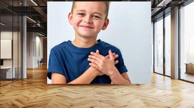 Close up of cute happy small boy isolated on white studio background hold hands at heart chest feel grateful, smiling little child pray thanking god high powers, faith concept Wall mural