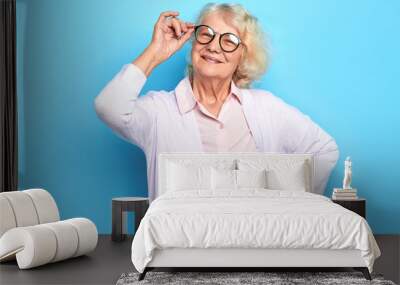 close up portrait of senior woman doctor in glasses with a hand on her hip standing in medical office.free time, spare time. isolated blue background. Wall mural