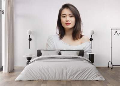 Close up studio shot of calm Asian young woman with healthy clean skin, gorgeous dark hair and expressive big eyes in white t-shirt looking at camera with calm and serious expression. Wall mural