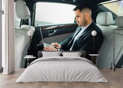 Confident man in tuxedo sit using laptop, working in car, man with beard Wall mural