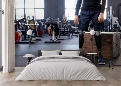 cropped shot of body of disabled man with prosthetic leg standing in modern gym preparing for weight training. copy space, blurred background. strength health care Wall mural