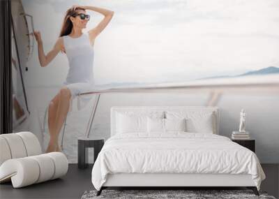 Dreaming caucasian woman in white dress wearing sunglasses sitting on railings of a luxury boat. Outdoors, lifestyle Wall mural