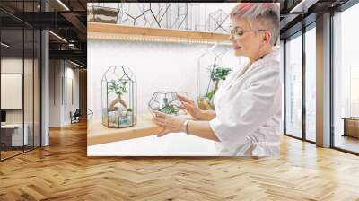 Elderly woman florist look after plants in office, work place. Woman wearing white suit in office full of plants. Light room Wall mural