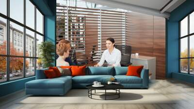 Female sales agent at the table desk telling about car features to cheerful couple of customers at car dealership office Wall mural