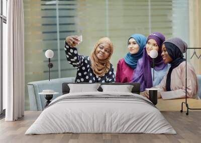 Four asian Muslim student girls sitting together, wearing hijabs and long traditional wear having fun after classes and taking selfie in college classroom Wall mural