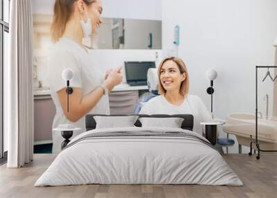 friendly doctor dentist examine teeth of caucasian young woman in casual wear, isolated in dentist office, using special medical equipment Wall mural