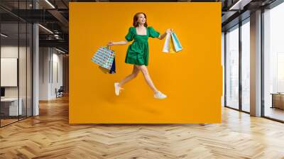 Full body photo of funny lady tourist walk shopping center carrying many packs, having good mood, best weekends, wearing dress isolated on yellow studio background, portrait Wall mural