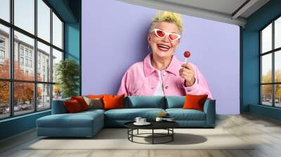 funny playfull cheerful old woman in pink stylish suit holding chup chups and posing to the camera. closeup portrait Wall mural