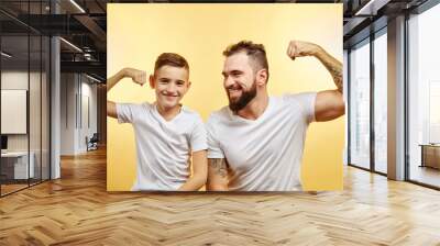 Handsome bearded father and his son looking at camera and smiling while show biceps Wall mural