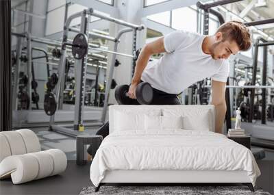 Handsome caucasian man doing biceps lifting with dumbbell on bench in crossfit studio Wall mural