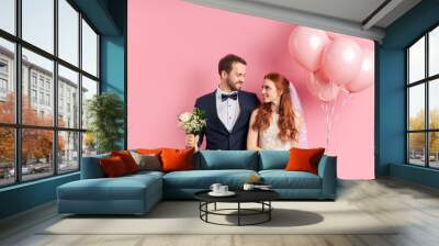 handsome man in tuxedo and redhaired woman in wedding dress look at each other with love. holding pi Wall mural