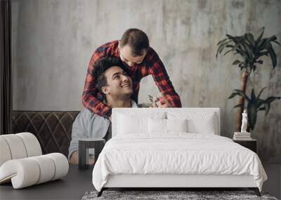 Joyful homosexual man makes a surprise with flowers for his male lover, while those one working on laptop at office chill out space Wall mural