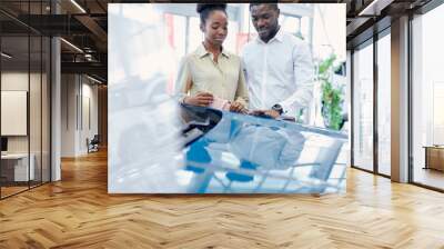 just imagine us on the road. portrait of happy african american couple checking out a car in modern dealership, they choose new car together Wall mural