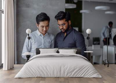 Mix raced couple of male business partners planning next sales period. Indian and Korean male colleagues in formal shirts and studying documents in the big office room. Business concept Wall mural