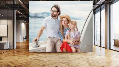 Outdoor portrait of happy family with 4-year old daughter on sailing boat at sunny summer day. European parents playing with kid on a bow of luxury yacht. Family, Marine Cruise and people concept Wall mural