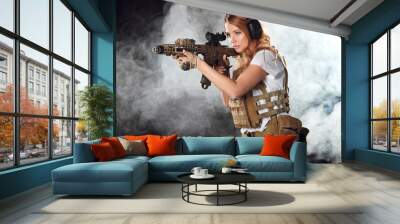 Portrait of a beautiful woman warrior in military outfit with firearm in hands, aiming at enemy, fighting in smoke from exploding shells at night Wall mural