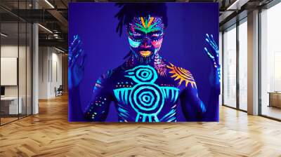 portrait of african man painted in fluorescent paint on face and muscular torso, studio shot with UV light. ethnic prints Wall mural