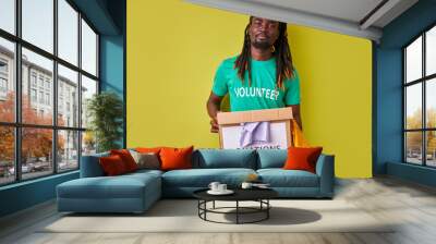 portrait of black afro volunteer man with box full of clothes, young male with dreadlocks engaged in charity, love helping others Wall mural