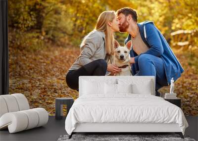 portrait of lovely couple in the forest, caucasian man and woman kissing, holding white pet dog in hands Wall mural