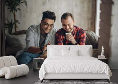 Romantic partners in love and business. Caucasian amused gay couple looking at laptop screen while resting in living room with loft interior. Dominant man wearing spectacles and and using laptop Wall mural