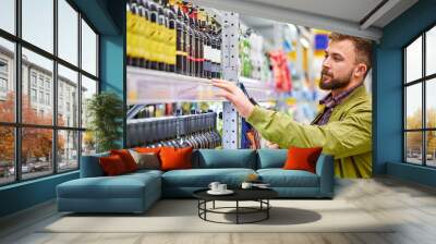 sale, consumerism, alcohol and people concept - young man with bottle of wine, choose the best and delicious one, look at shelf Wall mural