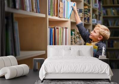 school boy taking books from shelves in library, with a stack of books in hands. child brain development, learn to read, cognitive skills concept Wall mural