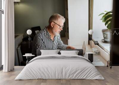 Senior man at home in front of laptop computer working. Freelancer, on line worker Wall mural