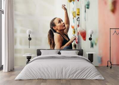 Side view of professional climber female at the rock climbing wall at the gym. Light background with copyspace Wall mural