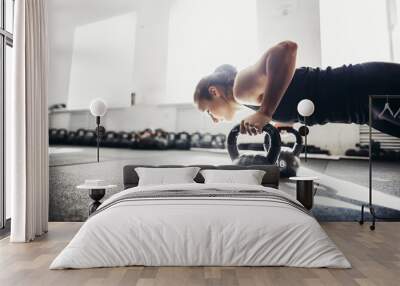 Slim brunette doing push-ups exercises on kettlebells. Cross fit training. focus on kettlebells Wall mural