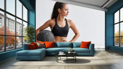 Slim caucasian cross fit woman with fitness ball stand in gym, look. White wall background Wall mural