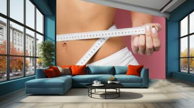 slim woman measuring her stomach using white measure tape after a diet isolated over pink background Wall mural