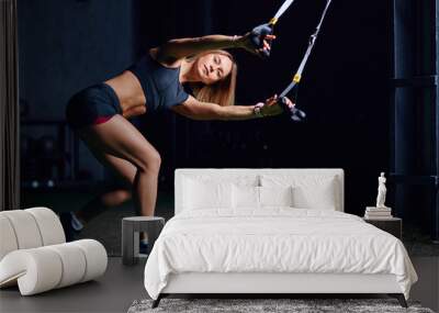 Sportive well-shaped young woman doing TRX straps exercise training at cross fit gym with loft interior, dark shadow studio lighting. Wall mural