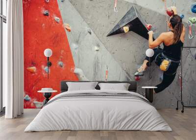 Sporty strong young woman in black outfit exercising in boulder climbing hall reaching new results, enjoying new challenges. Wall mural