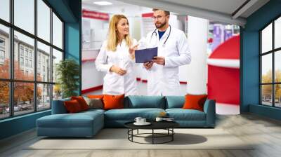 team of young caucasian chemists or druggists discussing medicines, check medical indications, in white medical gowns, at work place Wall mural