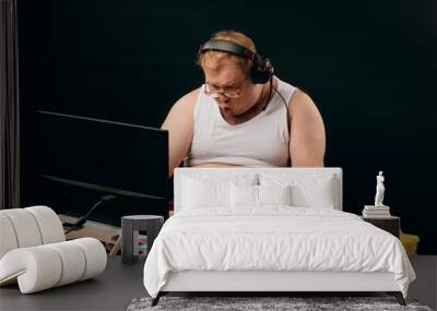 technology concept. funny young man in headset with pc computer playing game at home. isolated black background.studio shot Wall mural