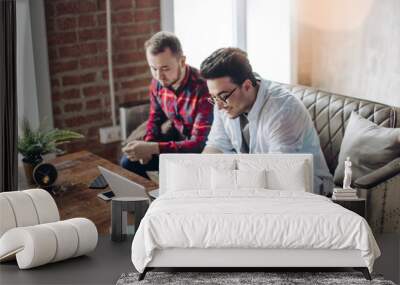 Two male buddies sitting in modern loft design office looking at laptop and discussing business ideas. Wall mural