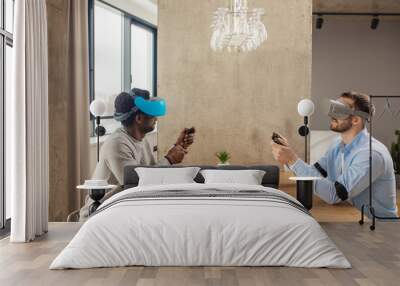 Two male entrepreneurs in casual clothing, sitting opposite each other at table in empty room, being busy with developing a project using virtual reality goggles Wall mural