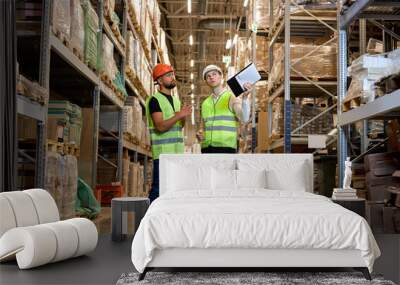 warehouse managers in work wear organizing distribution in warehouse storage area. Caucasian men in green uniform discuss product delivery, having talk. in retail Warehouse full of Shelves with Goods Wall mural