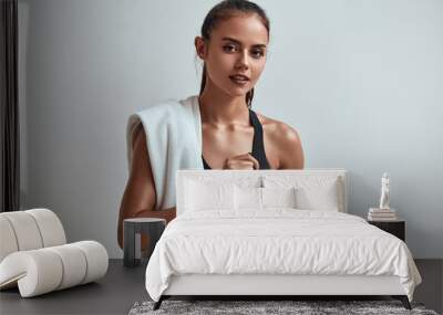 Young attractive woman in sportswear holding water bottle with towel on shoulders. Isolated in grey studio, room Wall mural