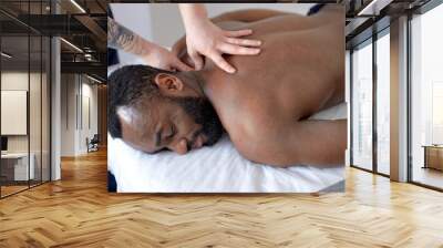 Young black man receiving back massage in spa wellness center. male patient is receiving treatment by professional therapist with strong hands. Body positive, harmony, healthy lifestyle Wall mural