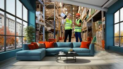 young Caucasian workers in uniform make an inventory management of products on shelves in warehouse, discuss together. Concept of good management system to support working with industrial business. Wall mural