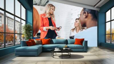 Young female expert in red jacket makes a presentation at a meeting in the office. Blonde woman sharing information with company of young friends. Wall mural