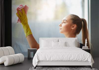 Young long haired girl cleaning panoramic window with yellow gloves. Wall mural