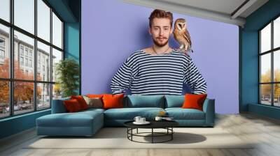 young man going to show tricks with an owl, isolated blue background, studio shot. clown having arest during working day Wall mural