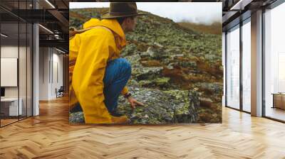 Young man in yellow raincoat and grren nat is sitting on cliff's edge and looking to misty valley bellow, scared man has noticed wild animal. copy space. close up side view photo Wall mural