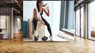 Young woman in leggins with towel on shoulders drinking water after fitness training Wall mural