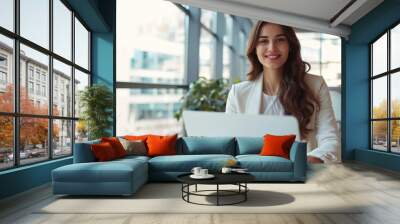 A happy businesswoman works on her laptop in a modern office Wall mural