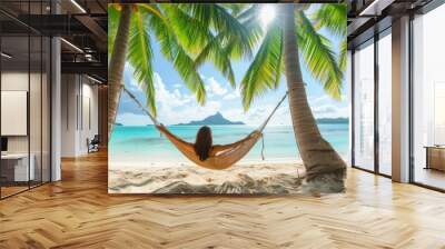 A young woman is relaxing in a hammock strung between two palm trees in a tropical paradise Wall mural