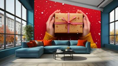 Hands holding a Christmas gift box with festive decorations, snow falling on a vibrant red background, perfect for a website design studio banner Wall mural